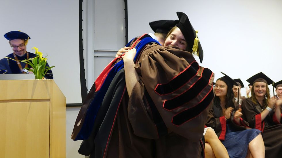 A PhD student and professor hug after bestowing her hood 