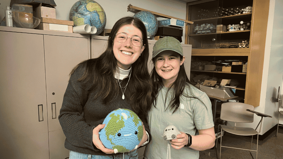 two students smile for a photo together, each holding a crocheted "birb"