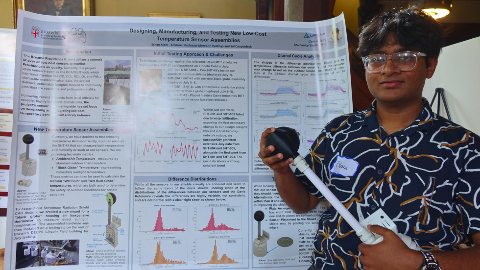 Eshan beside his poster holding a device from the project 