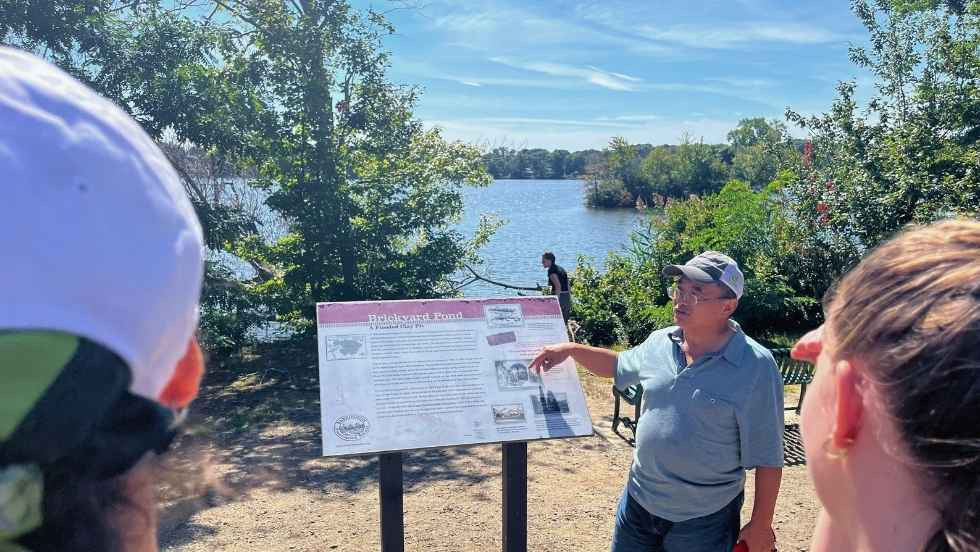 Professor Yongsong Huang reviewing a information marker beside a lake with students