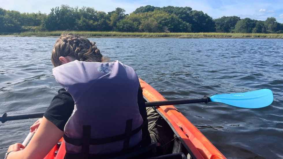 a student on a kayak in the middle of a lake taking a water sample 