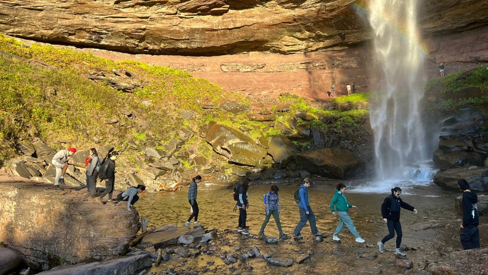 Students walking in front of a rocky waterfall