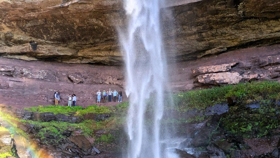 students waving from behind a waterfall 