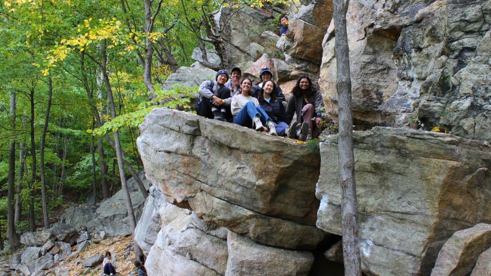 a group of students sitting together on top of a rocky cliff formation, smiling for the photo