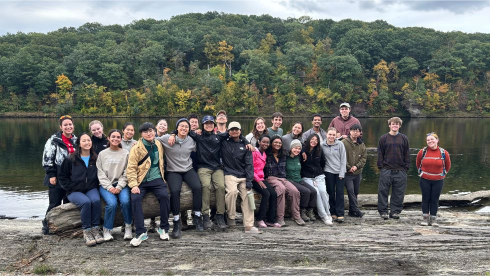 the field trip participants pose together for a group photo on the rocky shoreline 