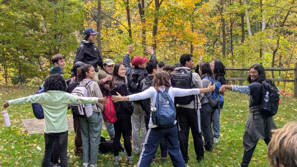 Students laughing in groups groups illustrating geologic-style formations, outdoors in a forest area