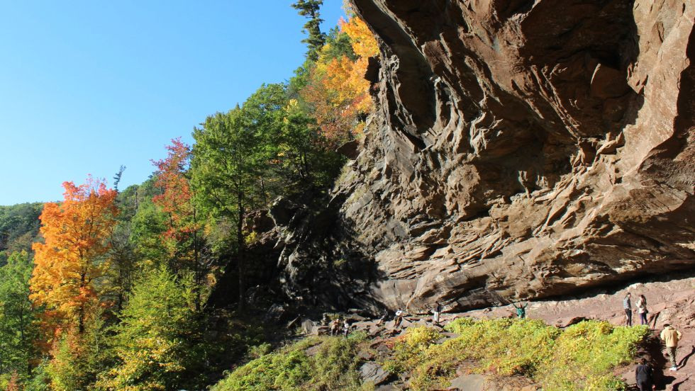 a wide view of a rocky cliff, with students waving to the camera underneath 